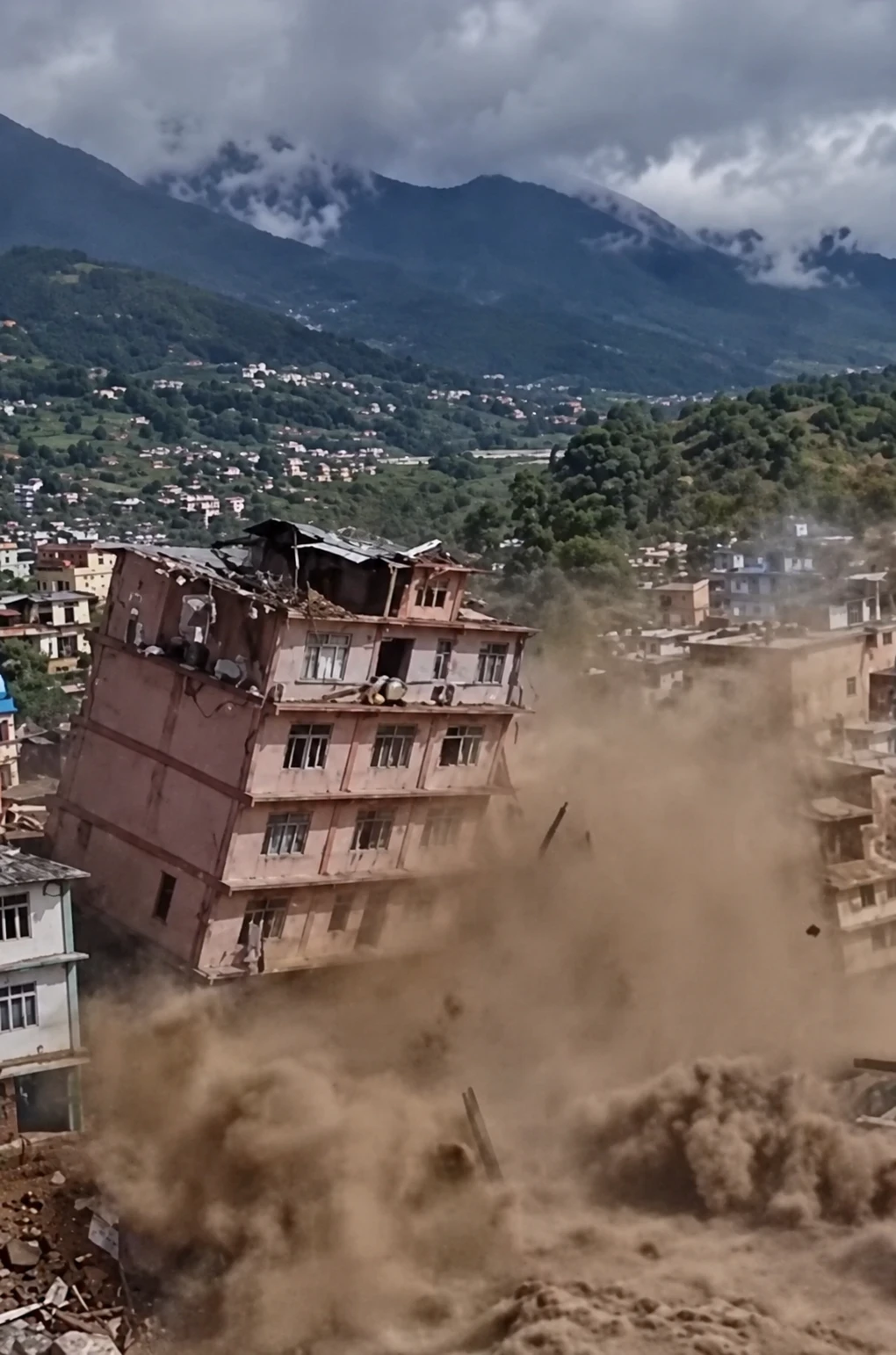 A multi-storey building partially collapsing amid clouds of dust in a built-up area