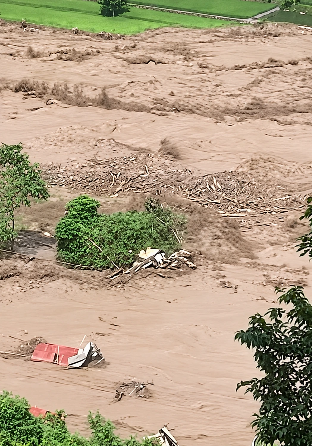 Floodwater covering farmland, carrying debris and the remains of damaged structures