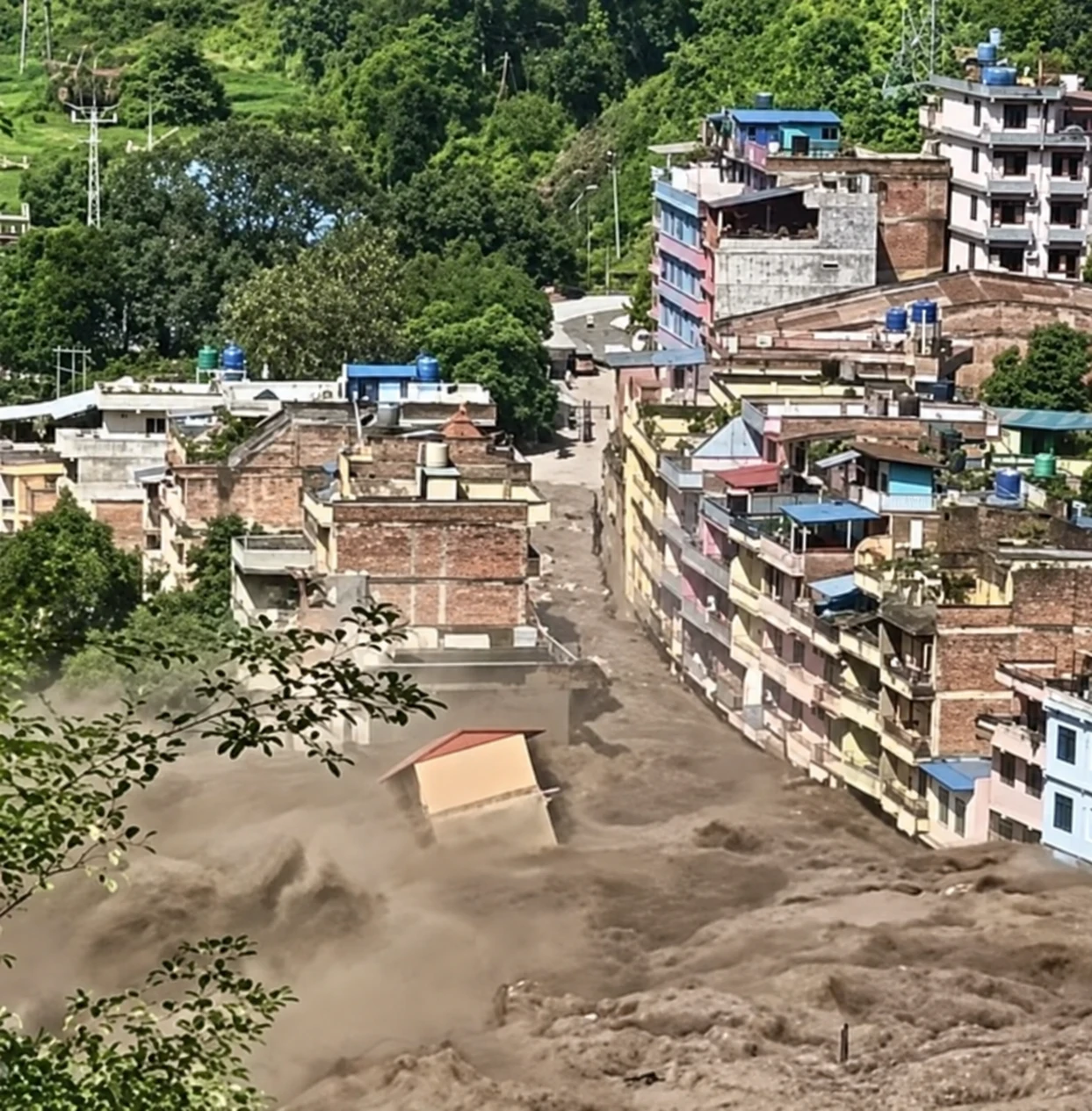 Thick mud and floodwater flowing between multi-storey buildings in a Nepalese town